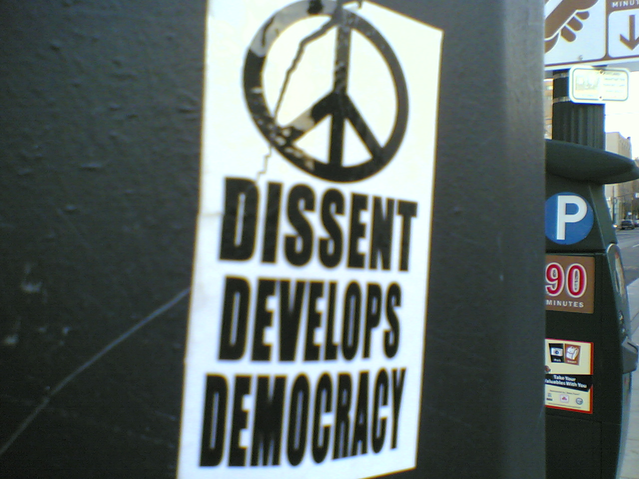 Sticker advocating dissent: "dissent develops democracy", accompanied by a peace symbol. Photo taken in Portland, Oregon. Photographer is Jason Wilson